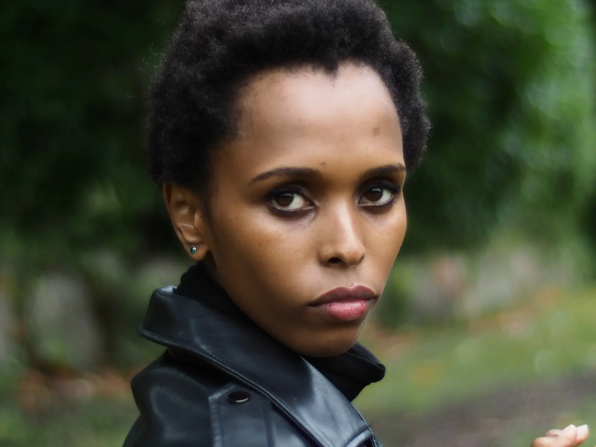 Woman with short natural hair in a black leather jacket looking over her shoulder