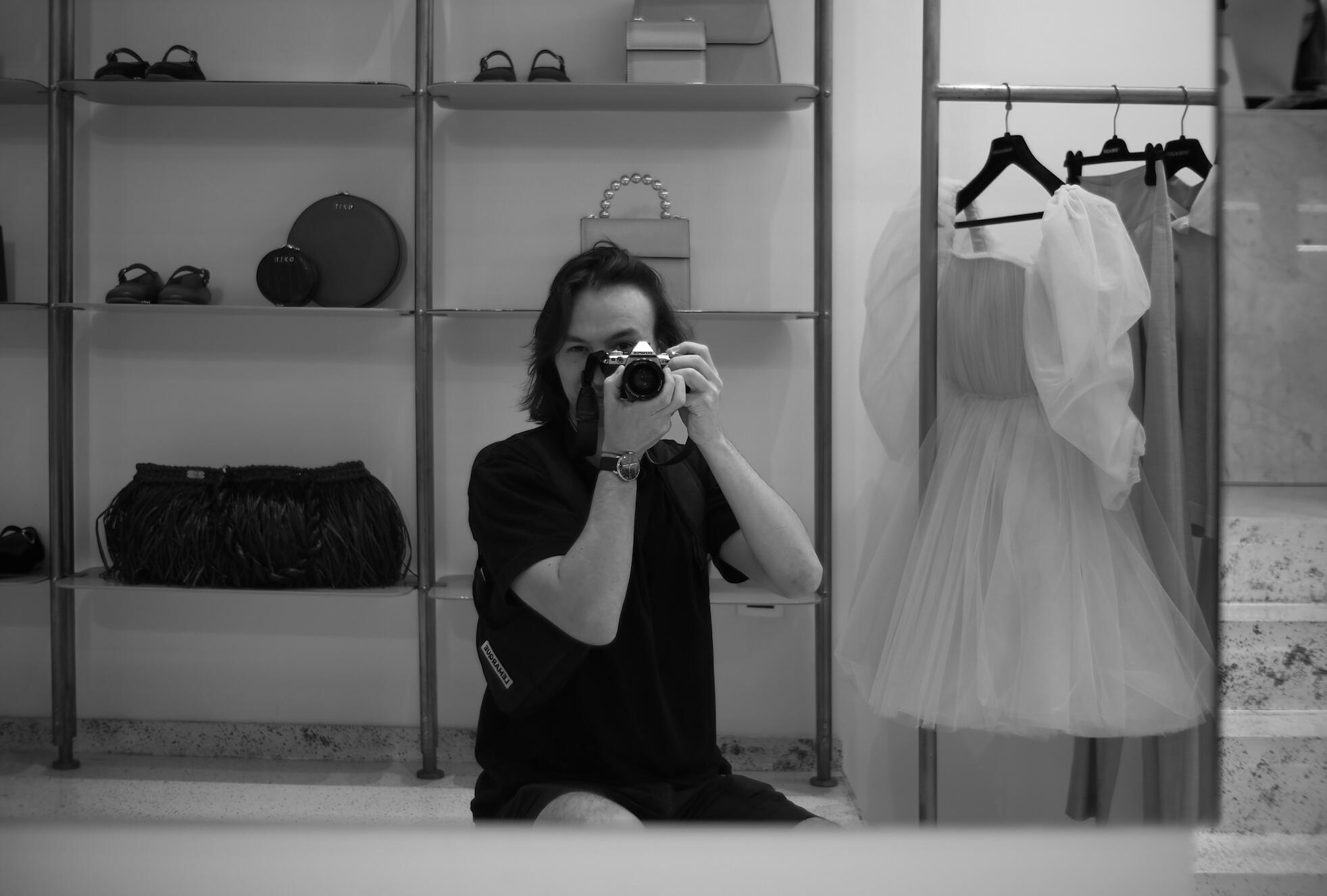 Black-and-white mirror selfie with a camera in a clothing boutique