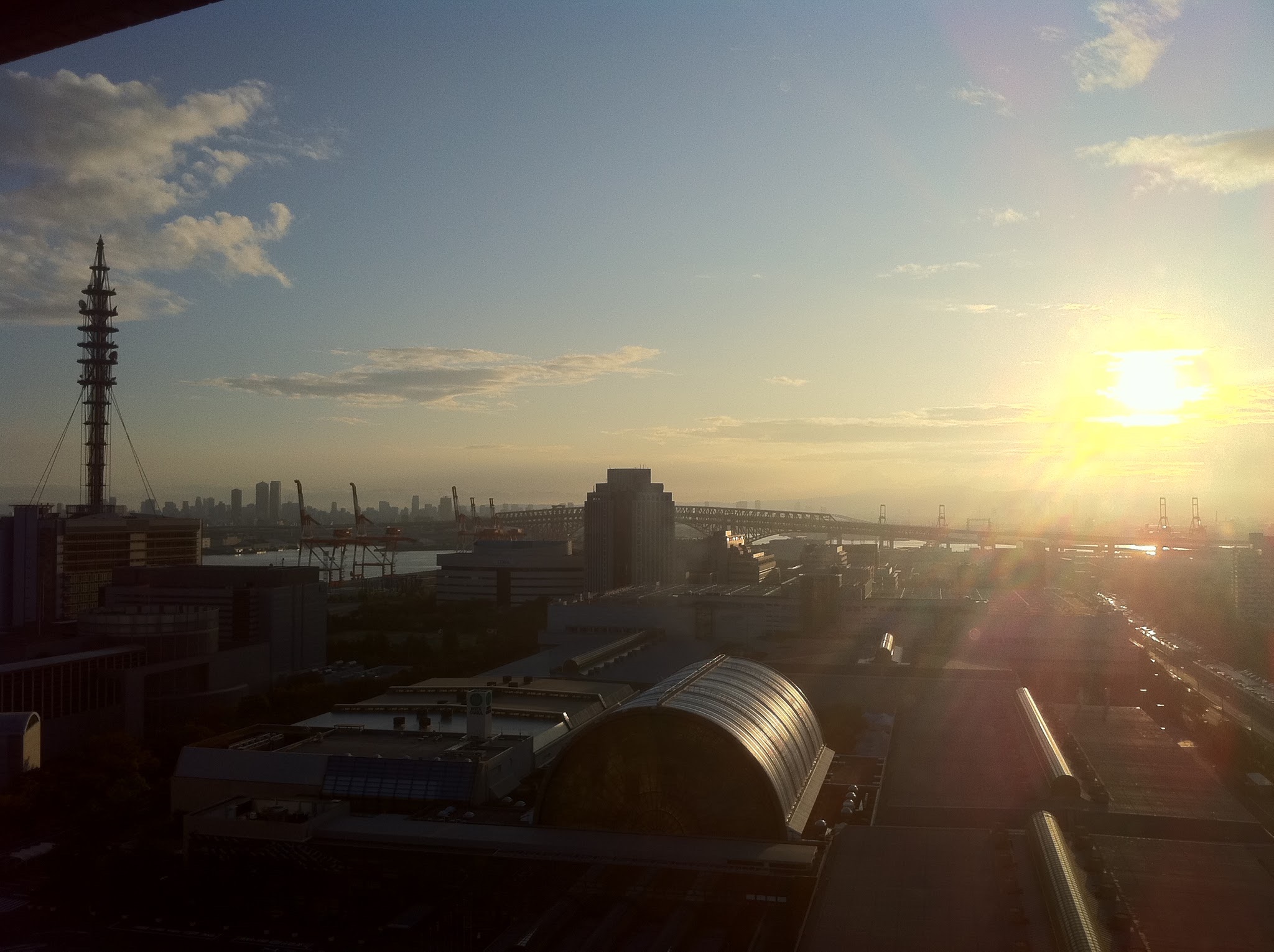 Low sun over a harbour with cranes, a truss bridge and a city skyline