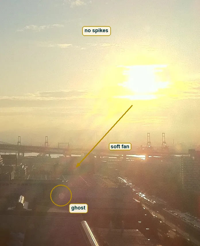 Close crop of the sun showing a soft fan of glare down and left, no star spikes, and a small faint ghost disc