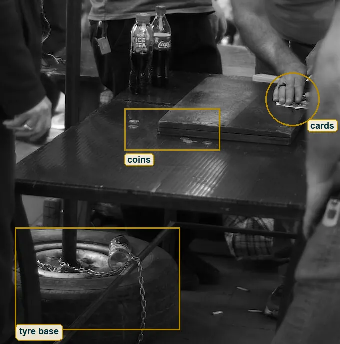 Crop of the low table with the cards under a hand, coins on the dark top and the tyre that holds the pole