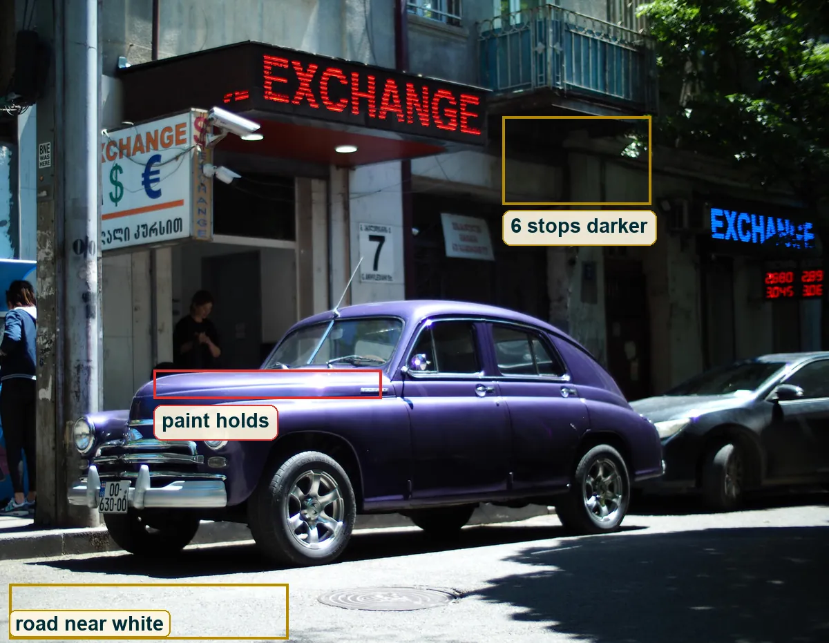 Full frame with boxes on the white road, the dark shaded wall and the purple bonnet