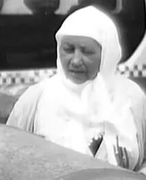 Crop of the older woman in a white headscarf looking down past the group