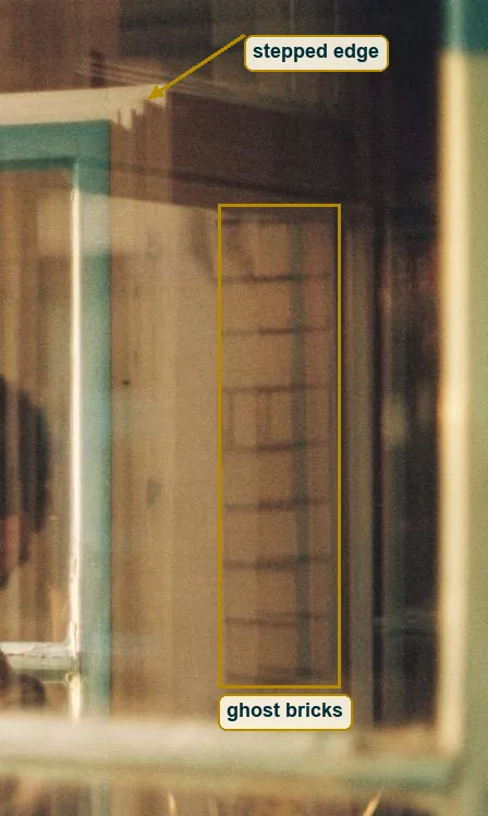Crop of the right pane where reflected brick courses and a stepped roof edge lie over the room
