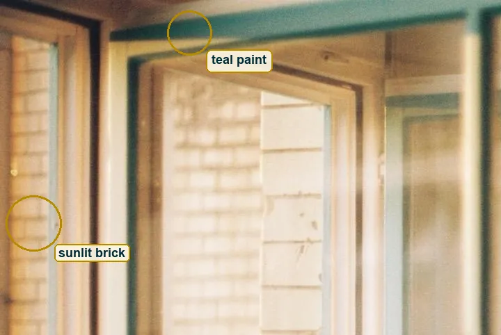 Crop of teal window paint beside cream brick turned amber by the sun