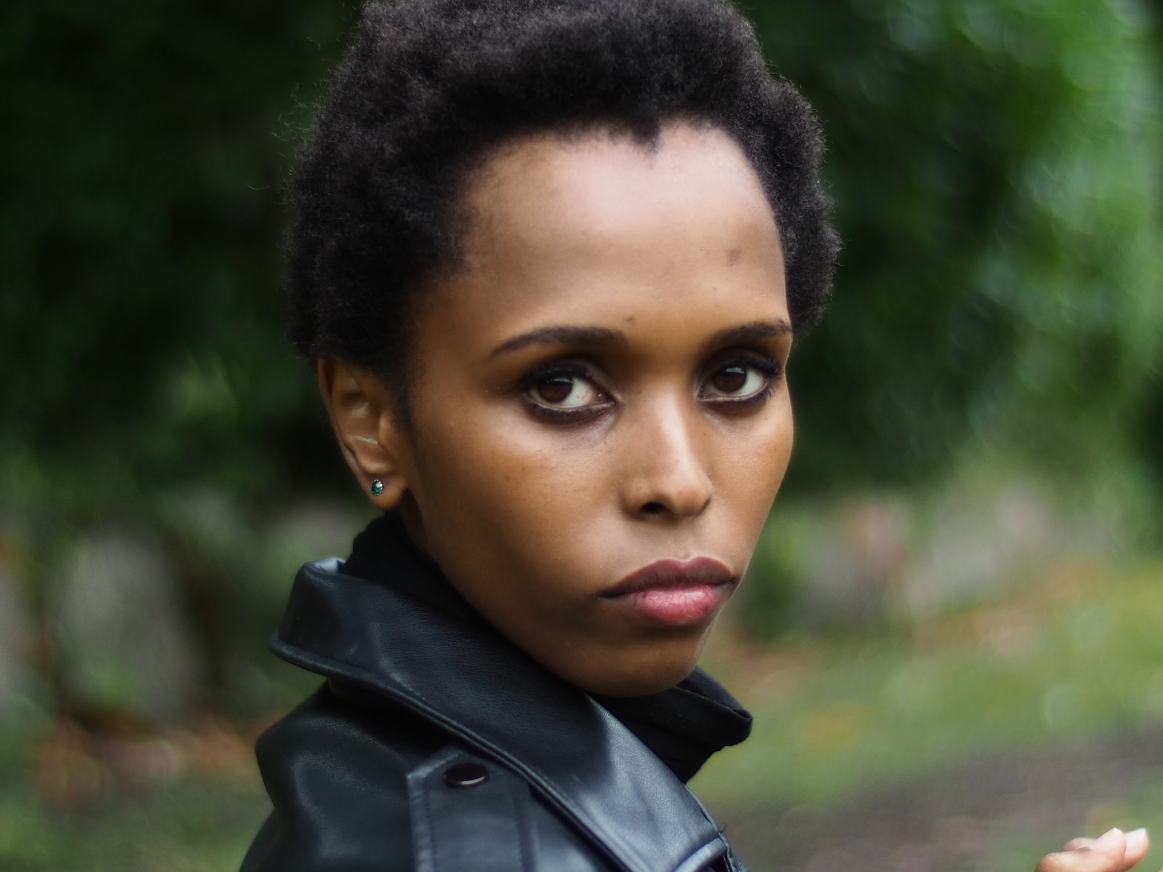 Woman with short natural hair in a black leather jacket looking over her shoulder